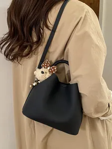Minimalist black bucket bag with plush bear charm worn with a stylish camel coat