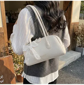 Gros plan du sac Boston en cuir crème avec nœud en dentelle et logo sur le côté