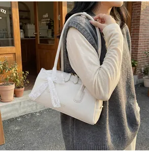Détail du sac Boston en cuir blanc cassé avec nœud en dentelle et logo doré