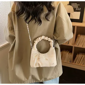 Detail of cream pleated handbag with lace bow, pearl charm, and metal chain strap