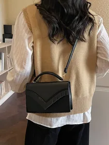 Minimalist black leather crossbody bag with V-shaped flap and gold hardware on model