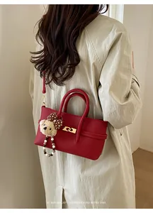 Detail view of red leather baguette bag with gold twist lock and cute plush bear charm