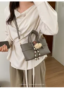 Detail of grey pebble leather handbag with decorative plush charm and beaded strap