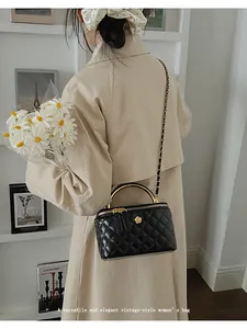 Close-up of black quilted box bag with golden metal handle and woven chain strap