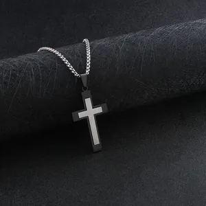 Detail view of two-tone steel cross pendant on a silver box chain over black texture