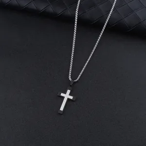 Detail view of a two-tone black and silver stainless steel cross pendant necklace on dark background