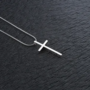 Macro di un ciondolo a croce in argento lucido su una sottile catena a serpente su sfondo nero