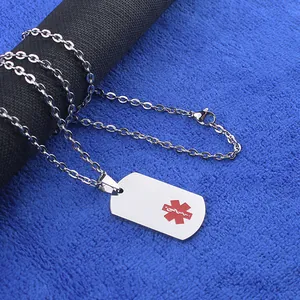 Détail d'un pendentif médical rectangulaire avec symbole de vie rouge sur chaîne acier