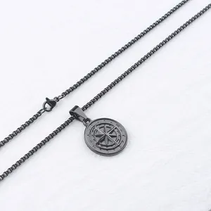 Detail shot of matte black compass coin pendant with matching bead chain on white fabric