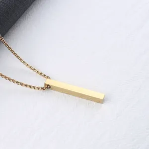 Close-up of polished gold rectangular bar pendant with box chain on white fabric