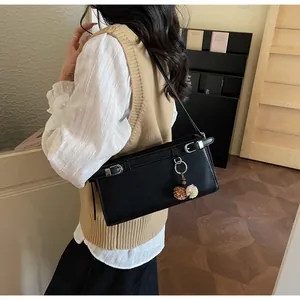 Détail d'un sac baguette noir avec boucles argentées et breloque pompon bicolore élégante