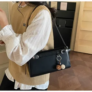 Détail du sac baguette en cuir noir avec boucles de ceinture et breloque pompon doux