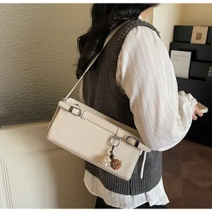 Détail du sac baguette en cuir crème avec sangles et breloques en peluche bicolores