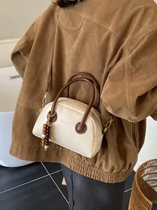 Sac baguette beige avec poignée marron et breloque perlée sur veste en daim