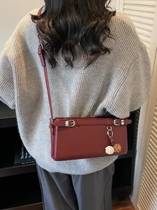 Sac baguette rectangulaire bordeaux minimaliste avec un pendentif fleur sur la bandoulière
