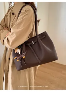 Detailaufnahme einer dunkelbraunen Tote Bag aus genarbtem Leder mit Charms und Schultergurt
