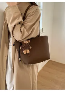 Detail of brown litchi pattern leather tote bag with a cute teddy bear charm
