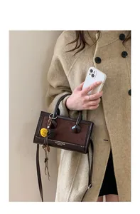 Détail du sac baguette en cuir marron foncé avec textures mixtes et pompon jaune décoratif