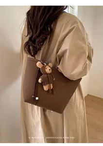 Detail of dark brown pebble leather tote bag with metal feet and cute teddy bear charm