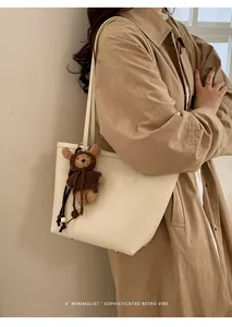 Detail of minimalist cream leather tote bag with a cute bear plush charm on shoulder strap
