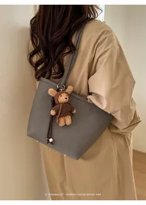 Chic grey lychee texture leather tote bag worn by a model with a cute teddy bear charm