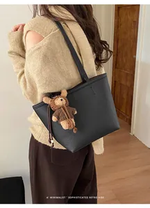 Detailed view of black litchi grain leather tote bag with cute plush bear charm decoration