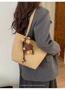 Close-up of khaki minimalist tote bag with a brown bear charm and long fringe tassel detail