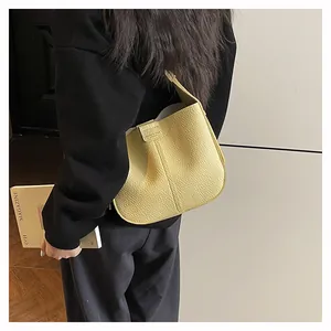 Détail du sac seau en cuir jaune pâle à texture litchi porté par le mannequin