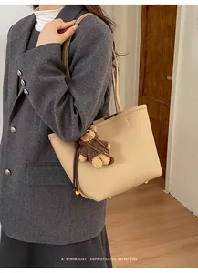 Close-up of khaki leather tote bag with lychee texture and cute bear bag charm accessory