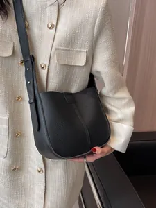 Sac seau minimaliste en cuir noir porté à l'épaule sur une veste en tweed chic