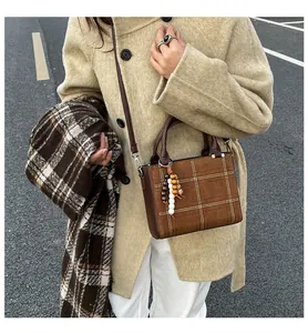 Detail of a brown suede crossbody bag with white stitching and wooden bead charm accessory