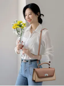 Brown and beige minimalist baguette bag with silver floral buckle held by a model