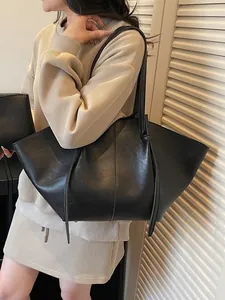 Sac fourre-tout minimaliste en cuir noir mat avec détails plissés porté à l'épaule
