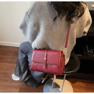 Gros plan d'un sac à bandoulière en cuir bordeaux avec boucle en métal sur modèle
