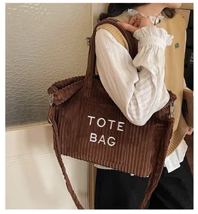 Detailed texture of brown corduroy tote bag with white TOTE BAG embroidery and strap