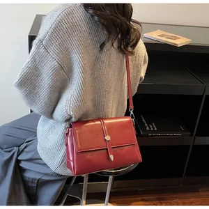 Détail du sac bandoulière en cuir bordeaux avec boucle métallique sur un mannequin chic