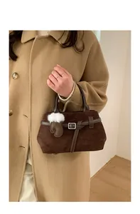 Détail du sac à main en daim marron avec pompon en peluche sur un manteau en laine