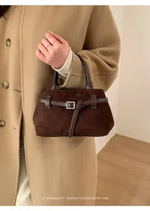 Gros plan d'un sac à main rétro en daim marron avec boucle argentée porté par un mannequin