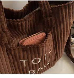 Detail of a brown corduroy tote bag showing the front pocket with a pink wallet inside