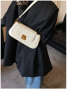 Detail einer cremeweißen Baguette-Tasche mit goldener Schnalle auf schwarzem Anzug