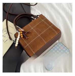 Detail showing brown plaid crossbody bag with colorful wooden beads and long leather strap