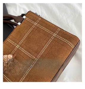 Close-up of brown suede bag with white quilted stitching and beaded handle detail