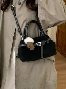 Petit sac noir à bandoulière avec charme gant marron porté sur un trench-coat