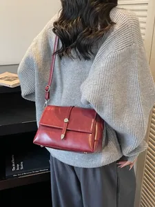 Sac à bandoulière élégant en cuir rouge foncé porté par un mannequin dans une bibliothèque