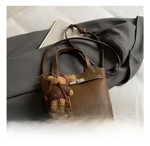 Macro detail of brown pebble grain leather bucket bag with metal buckle and teddy bear charm