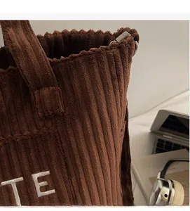 Detailed view of dark brown corduroy fabric with white embroidered text on the tote bag