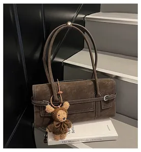 Detail of dark brown faux suede underarm bag with white stitching and bear charm