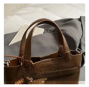 Detail of brown bucket bag with lychee grain texture, metal clasp, and woven charm