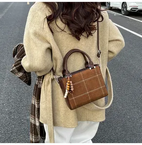 Close-up of brown suede crossbody bag with white stitching pattern and beaded charm