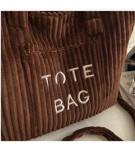 Detailed close-up of dark brown corduroy fabric and white TOTE BAG embroidery text